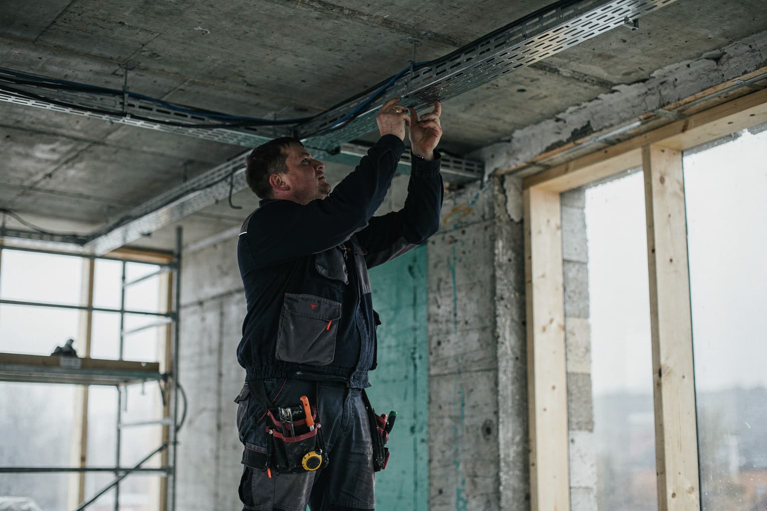 Electrician fitting cable trays in the ceiling of a building under construction